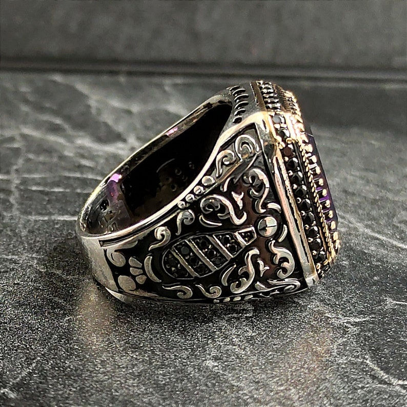 May include: A silver ring with an ornate design and a large, square, purple gemstone. The ring is set with smaller black gemstones around the edge of the stone.