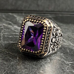 May include: A silver ring with an ornate design and a large, rectangular, purple gemstone set in a gold bezel.