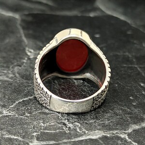 May include: A silver ring with a red oval gemstone set in a textured band.