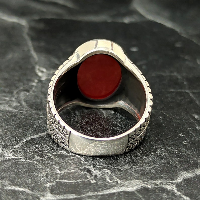 May include: A silver ring with a red oval gemstone set in a textured band.