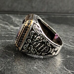May include: A silver ring with an ornate design and a large, square, purple gemstone. The ring is set with small black stones around the gemstone.