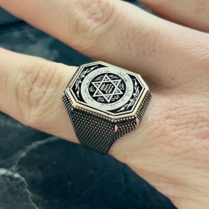 May include: Octagonal silver ring with a black and white design featuring a star of David and Arabic script.