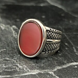 May include: A silver ring with a red carnelian stone set in a textured band.