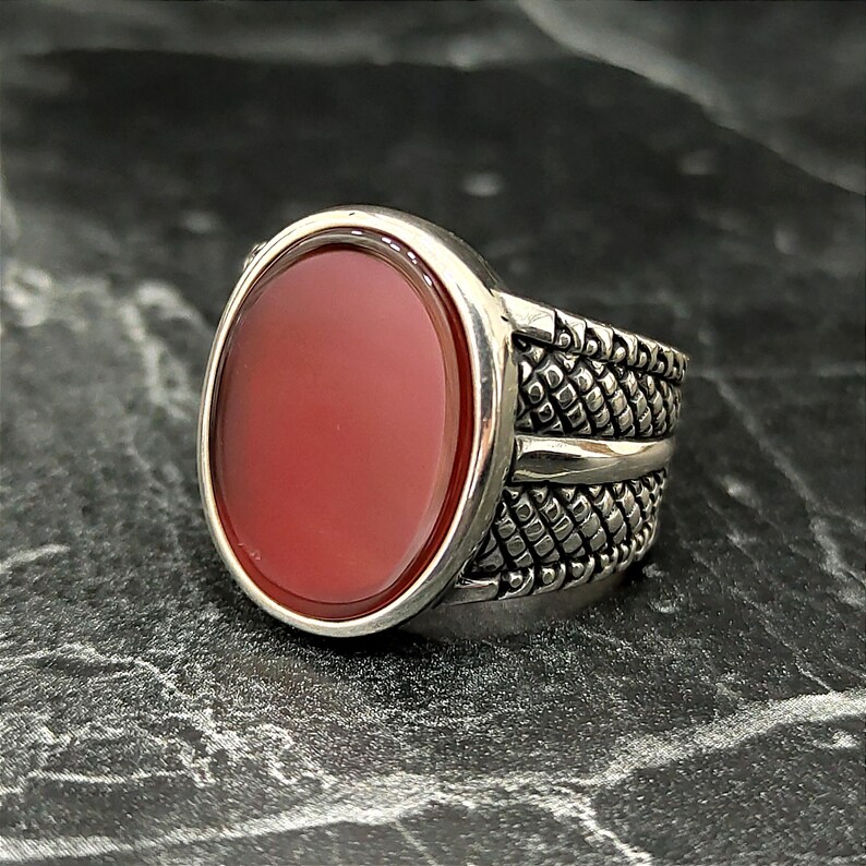 May include: A silver ring with a red carnelian stone set in a textured band.