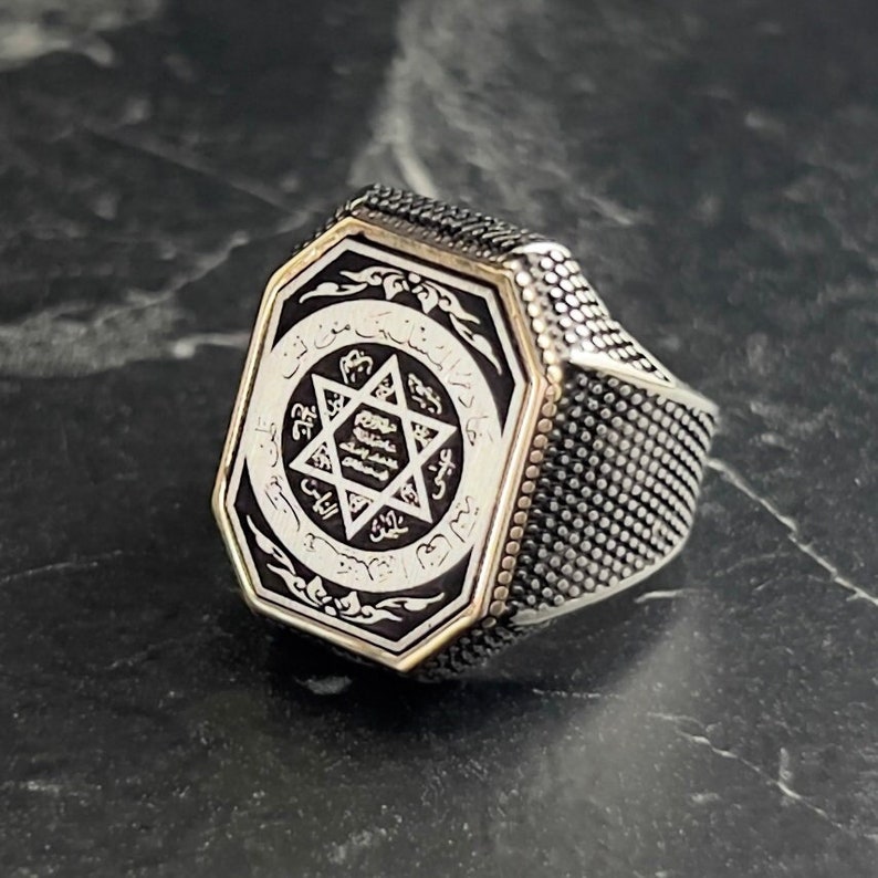 May include: A silver ring with a black octagonal stone featuring a white star of David and Arabic script.