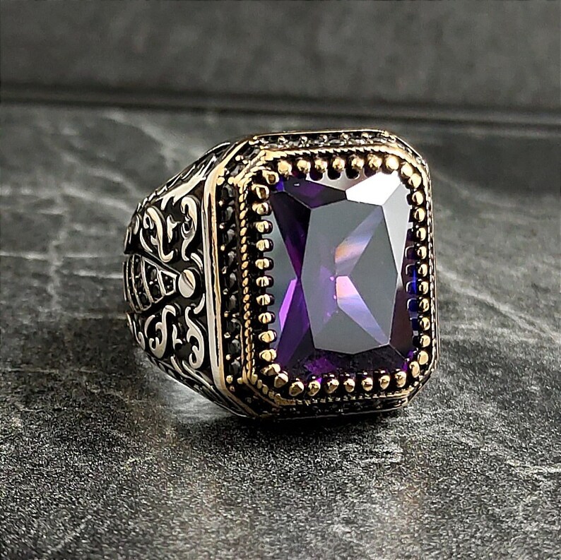 May include: A silver ring with an ornate design and a large, faceted purple gemstone set in a gold bezel.