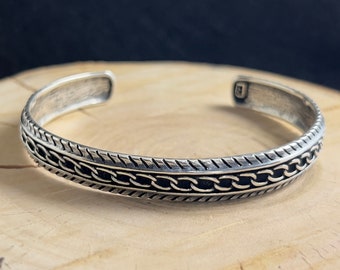 May include: A silver bracelet with a chain-link design and a textured edge.