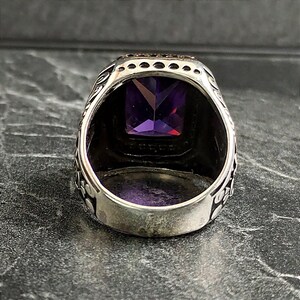 May include: A silver ring with an ornate design and a large, square, purple gemstone.