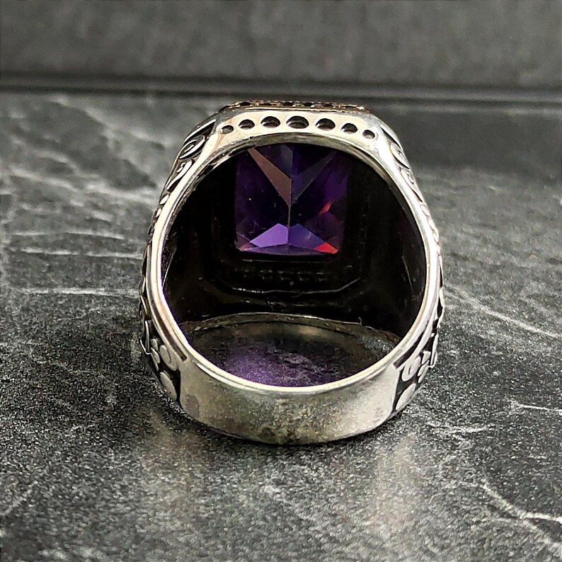 May include: A silver ring with an ornate design and a large, square, purple gemstone.