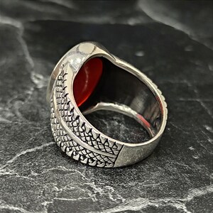 May include: A silver ring with a red gemstone set in a textured band.