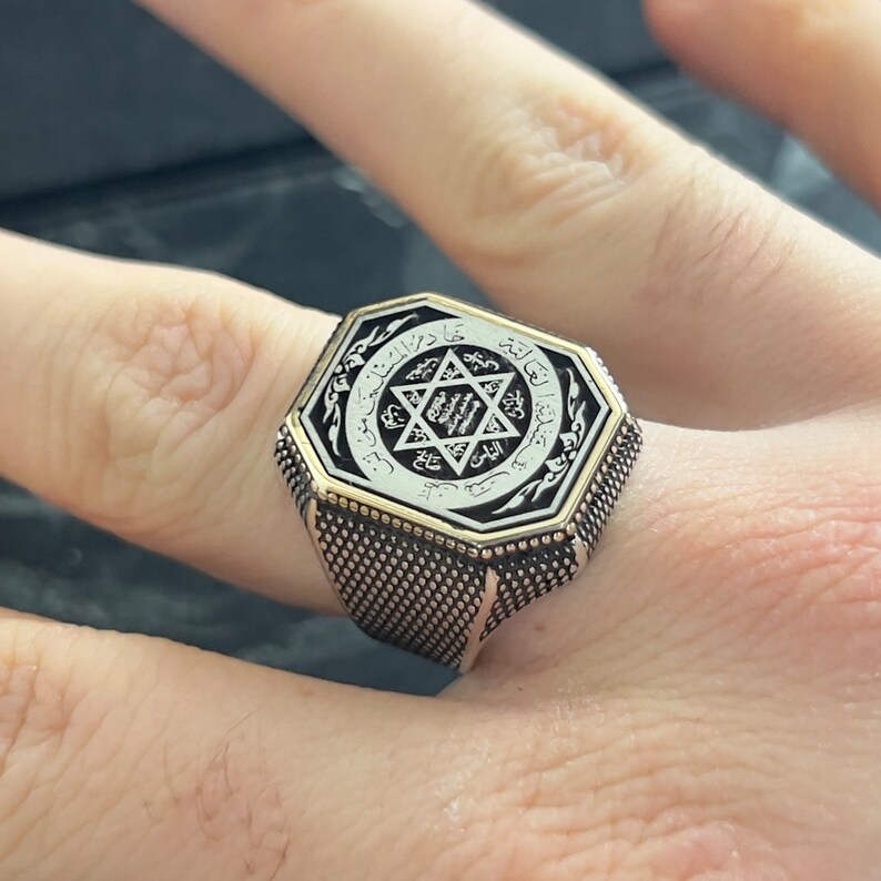 May include: A silver ring with an octagonal face featuring a black and white design of a star of David with Arabic script around it.