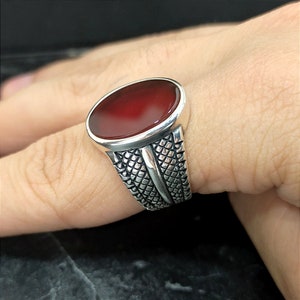 May include: A silver ring with a red oval gemstone set in a textured band.