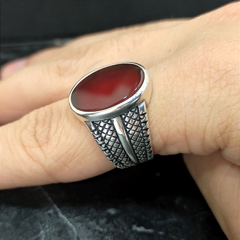 May include: A silver ring with a red oval gemstone set in a textured band.