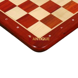 May include: A close-up of the corner of a wooden chessboard with alternating red and light wood squares. The board has a red border with white numbers and letters around the edge. The text "ANTIQUE" is printed in white on the red border.