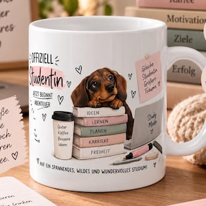 Peut inclure: Un mug en céramique blanche illustré d'un chiot teckel brun posé sur une pile de livres marqués Ideen, Lernen, Planen, Karriere et Freiheit. Le mug présente aussi une tasse de café, un ordinateur portable et du texte en allemand.