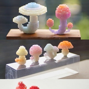 Könnte beinhalten: Eine Sammlung bunter, handgefertigter Pilzfiguren aus Perlen. Die Pilze sind in verschiedenen Größen und Formen, einige haben einen einzigen Hut, andere mehrere Hüte. Die Pilze werden auf einer weißen Oberfläche ausgestellt.