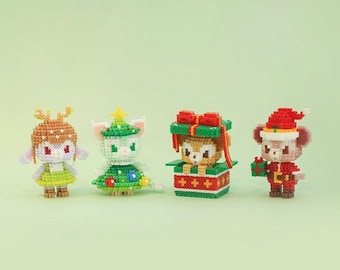 以下が含まれることがあります： クリスマスをテーマにしたピクセルアートの置物4つ。角のある白い鹿、緑のクリスマスツリー、赤と緑のギフトボックスに入った茶色のクマ、赤と白のサンタクロースの置物。