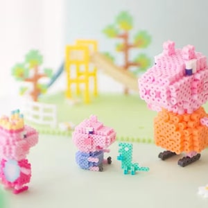 Könnte beinhalten: Eine Sammlung farbenfroher, pixeliger Spielfiguren, darunter eine rosa Schweinefigur mit einem orangefarbenen Kleid, ein blaues Schwein und ein grüner Dinosaurier. Die Szene spielt auf einer grünen Oberfläche mit einem Spielplatz im Hintergrund.
