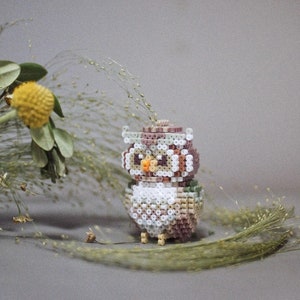 May include: A decorative owl figurine, crafted from small, colourful beads. The owl features a mix of white, brown, and green beads, with an orange beak and large eyes. A charming piece for home decor, it's a unique, handmade item.