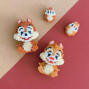 Könnte beinhalten: Drei Chipmunk-Figuren aus bunten Perlen. Der größte Chipmunk ist braun mit weißen Akzenten und einer roten Nase. Die beiden kleineren Chipmunks sind braun mit weißen Akzenten.