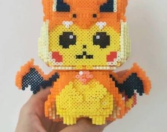 May include: A yellow and orange pixel art figure of a Pikachu wearing a Charizard costume. The figure has black wings and a red and yellow flame design on the back.
