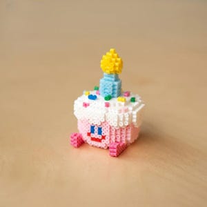 May include: A pink and white cupcake with a blue and yellow candle on top. The cupcake is decorated with colorful sprinkles and has a smiling face.
