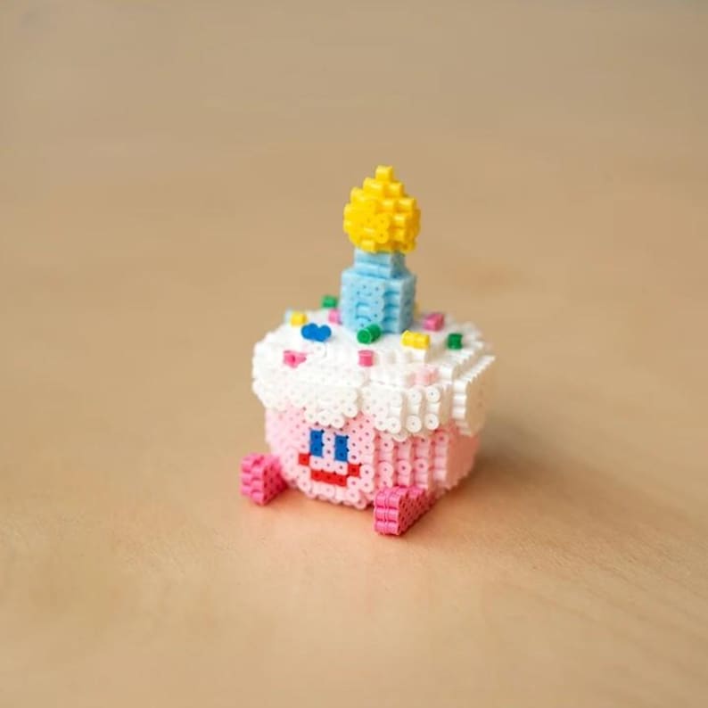 May include: A pink and white cupcake with a blue and yellow candle on top. The cupcake is decorated with colorful sprinkles and has a smiling face.