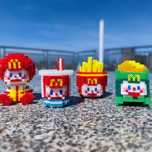 May include: Four small, colourful, bead-based figurines of a clown, a cup, fries, and a box. Each figurine has a cartoon face and the McDonald's logo.