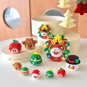 Pode incluir: Uma coleção de enfeites de Natal coloridos e pixelizados. Os enfeites incluem um boneco de neve, o Papai Noel, uma rena e uma coroa. Os enfeites são vermelhos, verdes, amarelos e brancos. O tema é festivo e natalino.