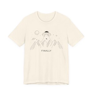 May include: Cream-colored t-shirt featuring a black line drawing of a UFO hovering over mountains, with a person being abducted. The word "FINALLY" is printed below the mountains. Stars, planets, and other celestial bodies are also depicted.