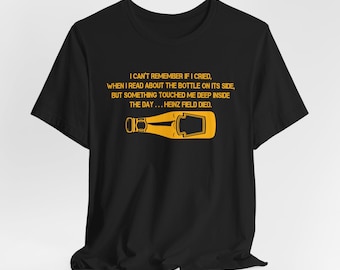 Op de afbeelding: Zwart T-shirt met een gele afbeelding van een ketchupfles en tekst. De tekst luidt: "I CAN'T REMEMBER IF I CRIED, WHEN I READ ABOUT THE BOTTLE ON ITS SIDE, BUT SOMETHING TOUCHED ME DEEP INSIDE THE DAY... HEINZ FIELD DIED."