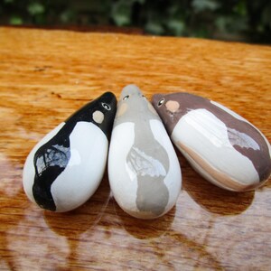 May include: Three ceramic penguin figurines, each painted in a different color scheme. One is black and white, one is gray and white, and one is brown and white.