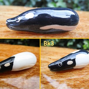 May include: Three ceramic figurines of a black and white animal, possibly a pangolin or an armadillo. The figurines are about 2 inches long and are painted in black, white, and a light brown color. The figurines are on a wooden surface.