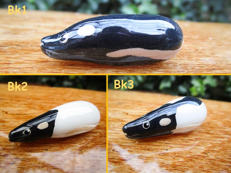 May include: Three ceramic figurines of a black and white animal, possibly a pangolin or an armadillo. The figurines are about 2 inches long and are painted in black, white, and a light brown color. The figurines are on a wooden surface.