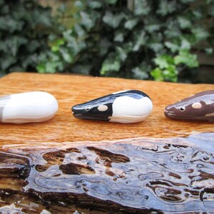 May include: Three ceramic animal figurines, each depicting a different type of rodent. The first is white with gray accents, the second is black and white, and the third is brown. The figurines are arranged in a row on a wooden surface.