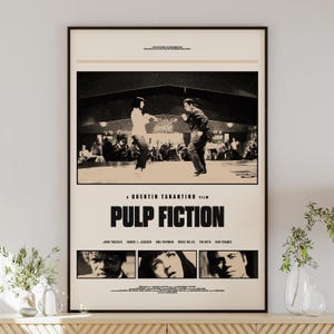 Pode incluir: Um cartaz de filme Pulp Fiction emoldurado apresentando uma cena em preto e branco de duas pessoas dançando. O cartaz inclui o título do filme em letras pretas em negrito, o nome do diretor e três retratos menores do elenco principal.