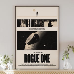 Può includere: Un poster incorniciato per "Rogue One: A Star Wars Story". Il poster presenta un design in bianco e nero con immagini del film, tra cui la Morte Nera e i personaggi. Il testo "WE HAVE HOPE. REBELLIONS ARE BUILT ON HOPE." è visibile.