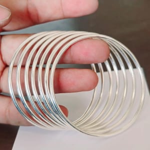 May include: A set of ten silver bangles, stacked and arranged in a circular pattern. The bangles are smooth and shiny, with a polished finish.