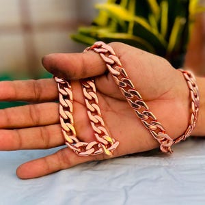 Puede incluir: Un collar de cadena de cobre con un diseño de eslabones de curb. La cadena es gruesa y tiene un acabado brillante.