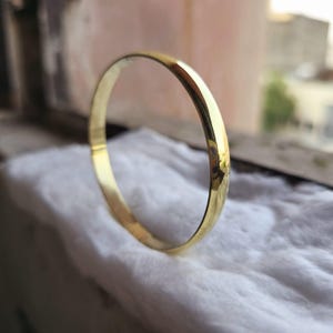May include: A gold bangle bracelet with a smooth, rounded surface.