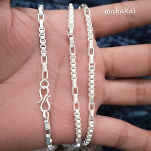 Könnte beinhalten: Eine silberne Halskette mit rechteckigem Kettenglied-Design. Die Halskette wird auf einer Hand präsentiert, die die komplizierten Details der Kette und den S-Haken-Verschluss zeigt. Das Wort "mahakal" steht in der oberen rechten Ecke.