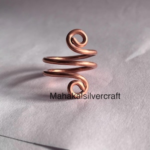 May include: A copper wire ring with a spiral design. The ring is made from a single piece of wire that is twisted and shaped into a spiral. The ring is a simple and elegant design.