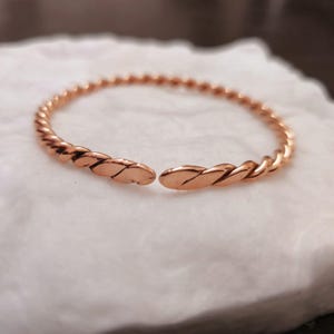 May include: A rose gold twisted bangle bracelet. The bracelet is open and has a simple design.