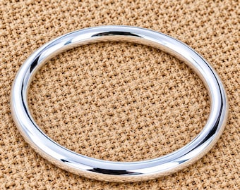 May include: A polished silver-tone metal ring with a smooth, rounded surface and a circular shape. The ring features a high-shine reflective finish that catches the light, creating bright highlights along its curved, continuous band structure.