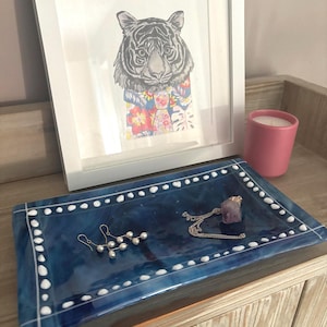 May include: A blue glass tray with a white dotted border. The tray is filled with jewellery, including a silver necklace with a purple stone pendant, a pair of silver earrings, and a strand of pearl-like beads.