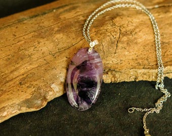 May include: A silver chain necklace with a large oval amethyst pendant. The pendant is a deep purple color with swirls of white and black.