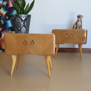 May include: Two wooden bedside tables with curved legs and brass handles. The tables are light wood with a chevron pattern.