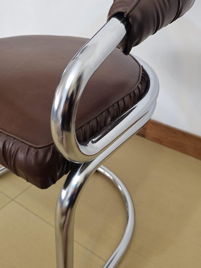 May include: A brown leather chair with a chrome frame. The chair has a curved back and a round seat. The chair is in good condition.