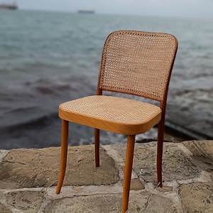 May include: A wooden chair with a woven cane seat and back. The chair is sitting on a stone patio with green grass in the foreground.