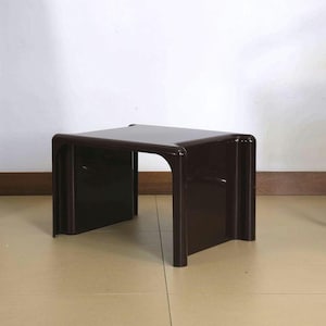 May include: A dark brown, square side table with rounded corners. The table has a simple, modern design and is made of a solid, glossy material. The table is approximately 18 inches wide, 18 inches deep, and 16 inches tall.